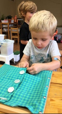 Lyonsgate Montessori student learning to use buttons using the Large Button Frame material.
