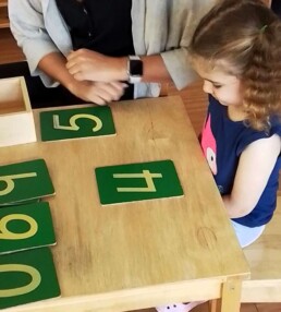 Montessori student beginning work with Sandpaper Numbers to learn letter shapes.