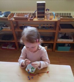 Montessori student during the first day back to school, September 2023. Threading beads for coordination and dexterity development.