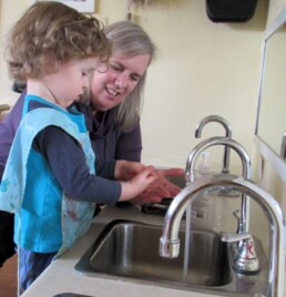 Lyonsgate Montessori Toddler student washing hands after painting.
