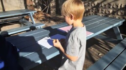 Lyonsgate Montessori Elementary student writing alliterative sentences outdoors on a warm, sunny fall day.