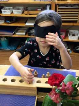 Lyonsgate Montessori Casa student developing sensory skills by using the Cylinder Blocks material while blindfolded.