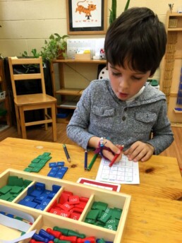 Lyonsgate Montessori Casa student working on the Montessori Stamp Game to learn addition.