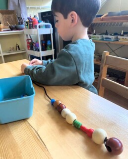 Lyonsgate Montessori Casa student threading beads.