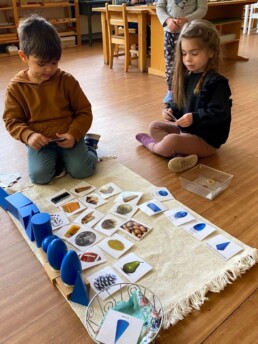 Lyonsgate Montessori Casa students sorting object cards into categories with the Montessori Geometric Solids.