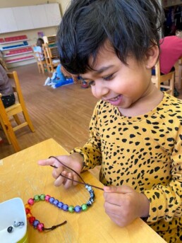 Lyonsgate Montessori Casa student threading beads to develop fine motor skills.