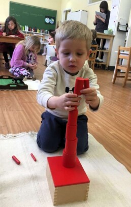 Lyonsgate Montessori Casa student working with the Montessori Knobless Cylinders to build a tower, develop motor skills and focus, and learn about balance, comparative volume, and built-in error control.