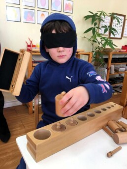 Lyonsgate Montessori Casa student working with the Montessori Cylinder Blocks material, blindfolded.
