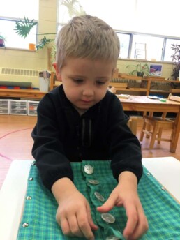 Lyonsgate Montessori Casa student practicing buttons with a Montessori Dressing Frame.