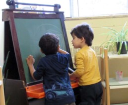 Lyonsgate Montessori Toddler students working together on the chalkboard.