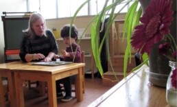 Lyonsgate Montessori Toddler student working with his teacher in their plant and flower filled classroom.