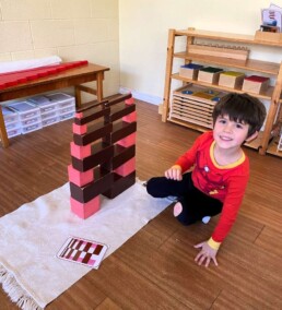Lyonsgate Montessori Casa student engaging in an extension activity with the Montessori Pink Tower and Brown Stairs materials, recreating the pattern on the card.