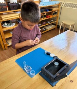 Lyonsgate Montessori School Casa student working with the Montessori Boxes and Bottles activity to develop motor skills and dexterity.