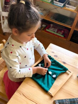 Lyonsgate Montessori School Casa student developing independence with a Montessori Dressing frame material.