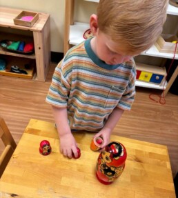 Lyonsgate Montessori School Toddler student exploring the wonder of a nesting doll, and figuring out how to take it apart and put it back together.