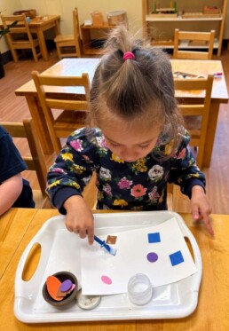 Lyonsgate Montessori School Toddler student pasting foam shapes to develop motor skills and creativity.