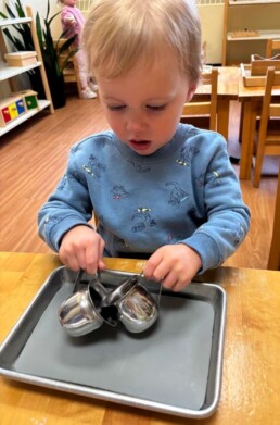 Lyonsgate Montessori Toddler student building motor skills and concentration by pouring popcorn from one jug to another.