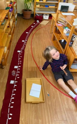 Lyonsgate Montessori School Casa student working with a Montessori Bead Chain material to learn multiplication tables and to have a visual and tactile experience of squares and cubes of numbers.