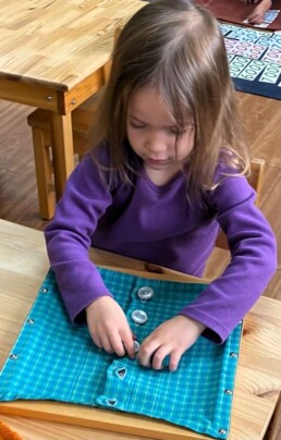 Lyonsgate Montessori School Casa student working with a Montessori Dressing Frame material -- the button frame in this case.