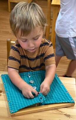 Lyonsgate Montessori School Casa student working with a Montessori Dressing Frame materials to develop independent dressing skills.
