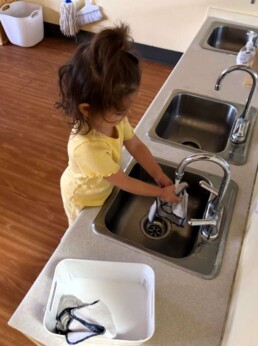 Lyonsgate Montessori School Toddler student preparing facecloths for lunch time for hand and face wiping to learn self-care after a meal.