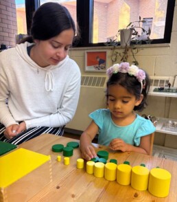 Lyonsgate Montessori School Casa student receiving a presentation of the Montessori Knobless Cylinders sensorial material that help refine visual discrimination of diameter and height.