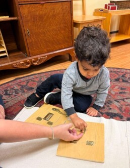 Lyonsgate Montessori School Toddler student being shown the locks and latches activity to develop motor and problem solving skills.