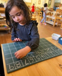 Lyonsgate Montessori School Casa student practicing writing the numbers 0-9 on a chalkboard.