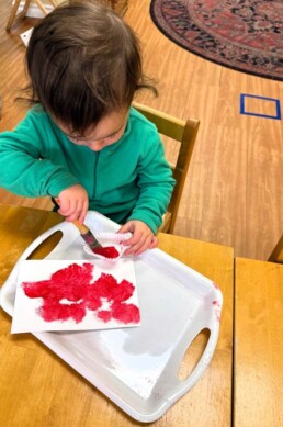 Lyonsgate Montessori School Toddler student exploring his creativity through painting with a brush while also working on wrist movement.