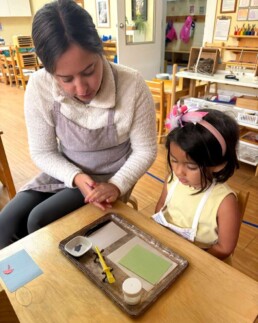 Lyonsgate Montessori School Casa student receiving a presentation of the Montessori Pasting activity, which is both creative and builds fine motor skills.