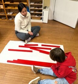 Lyonsgate Montessori School Casa student receiving a presentation of the Montessori Red Rods material to develop perception of length and to introduce base math language and concepts.