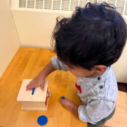 Lyonsgate Montessori School Toddler student learning to put an object into a slot and pull the draw out to see his work.