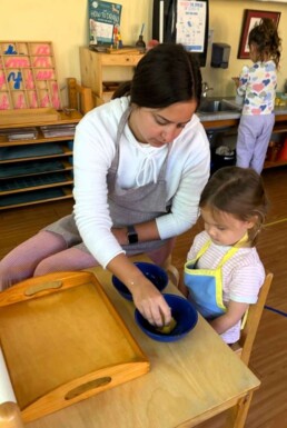 Lyonsgate Montessori School Casa student receiving a presentation of the Montessori Squeezing a Sponge activity to help build hand strength and concentration.