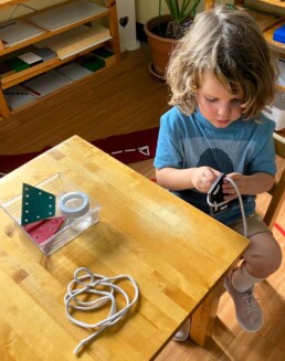 Lyonsgate Montessori School Casa student building focus and fine motor control with a threading activity.