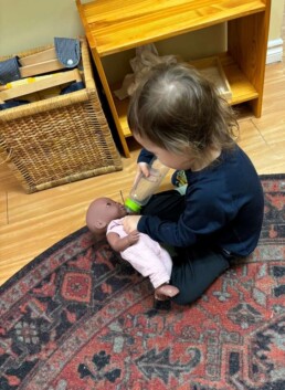 Lyonsgate Montessori School Toddler student feeding the baby a bottle and working on practical life skills on how to care for someone.