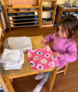 Lyonsgate Montessori School Casa student supporting the classroom by folding clean cloths, and building motor skills and focus.