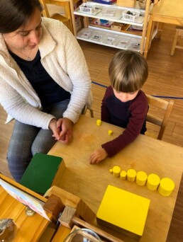 Lyonsgate Montessori School Casa student receiving a presentation of the Montessori Knobless Cylinders material.