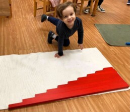 Lyonsgate Montessori School Casa student happily working with the Montessori Red Rods material to develop perception of length and receive an intuitive introduction to the decimal system and addition.