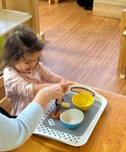 Lyonsgate Montessori School Toddler student helping to prepare snack items for her class.