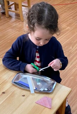 Lyonsgate Montessori School Casa student working at the Montessori Snippets activity to learn how to use scissors while developing fine motor skills and concentration.