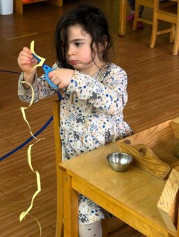 Lyonsgate Montessori School Casa student building visual and fine motor control skills, and focus, by using scissors to cut along a spiral line.