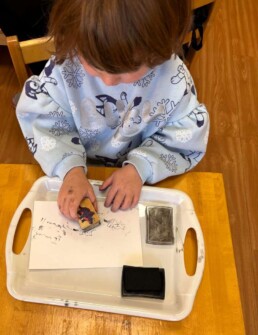 Lyonsgate Montessori School Toddler student learning to use a stamp and inkpad for creativity, motor control, and handwashing practice.