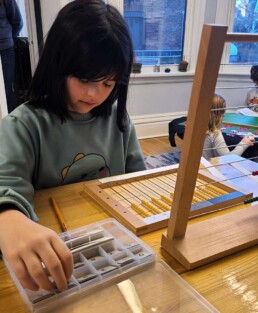 Lyonsgate Montessori School Elementary student working with the Montessori Flat Bead Frame material that supports the transition from concrete to abstract work with numbers.