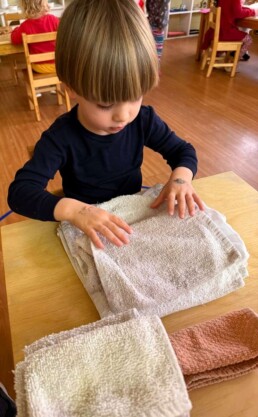 Lyonsgate Montessori School Casa student folding cloths to support his classroom environment while building focus and motor skills.