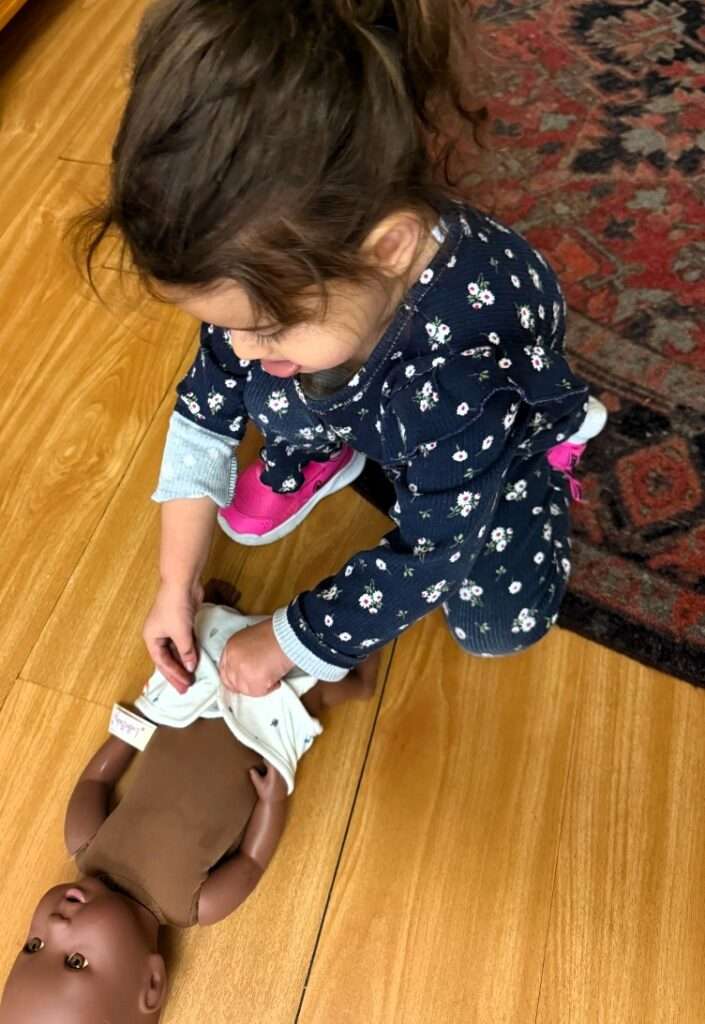 Lyonsgate Montessori School Toddler student getting ready for siblings by practicing putting on a diaper.