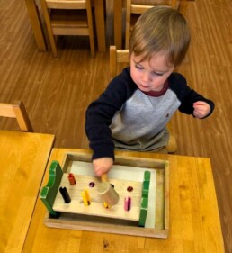 Lyonsgate Montessori School Toddler student building motor skills with a hammer and nail/peg activity.