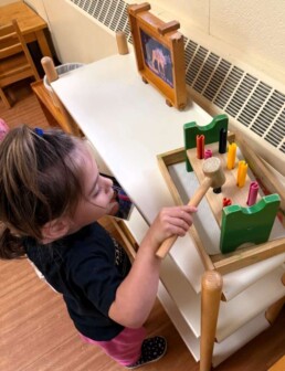 Lyonsgate Montessori School Toddler student building hand-eye-brain coordination with a hammer and nails activity.