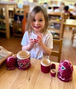 Lyonsgate Montessori School Casa student exploring a nesting doll, which is a motor development activity, a cultural material, and introduction to scientific taxonomy at different ages in Montessori.