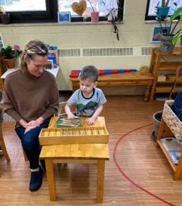 Lyonsgate Montessori School Casa student receiving a presentation of the Montessori Spindle Box material that relates visual, tactile, material quantities to number symbols.