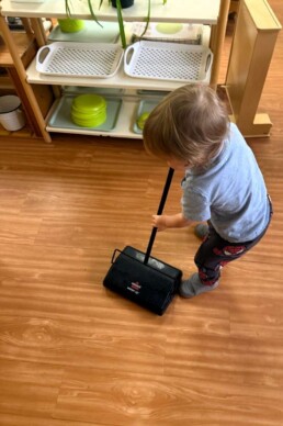 Lyonsgate Montessori School Toddler student helping to care for the classroom by cleaning the floor (and building strength, balance, and coordination).
